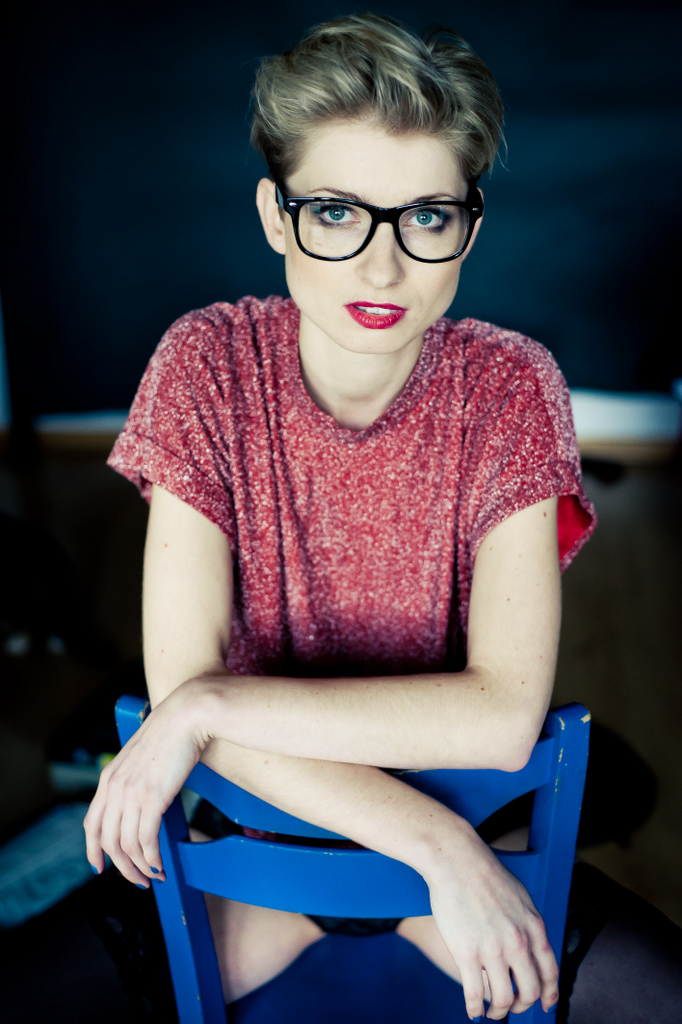 dziewczyna w okularach w czerwonej bluzce siedzi na niebieskim krześle