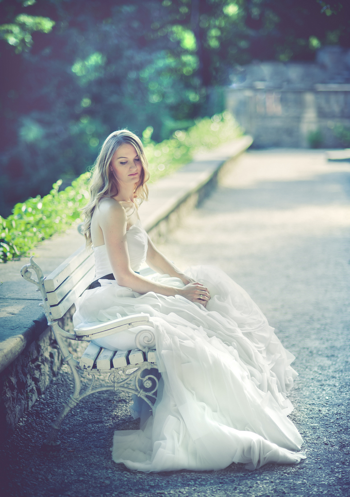 Kobieta w białej sukni siedząca na ławce