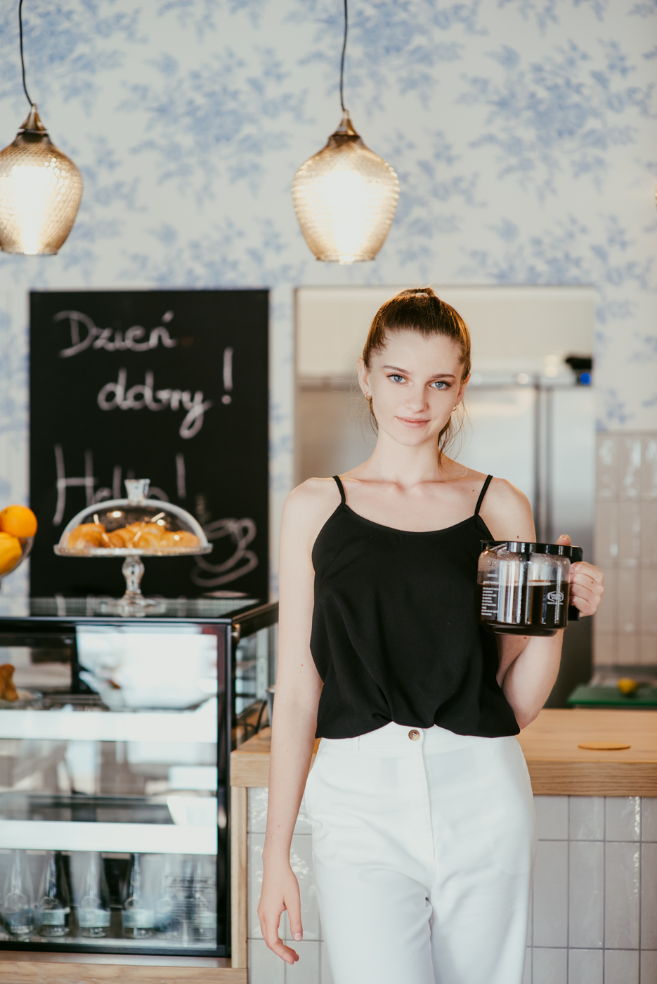sesja komercyjna. zdjęcia przedstawia młoda kobietę w kawiarnianym wnętrzu niosącą dzbanek z kawą