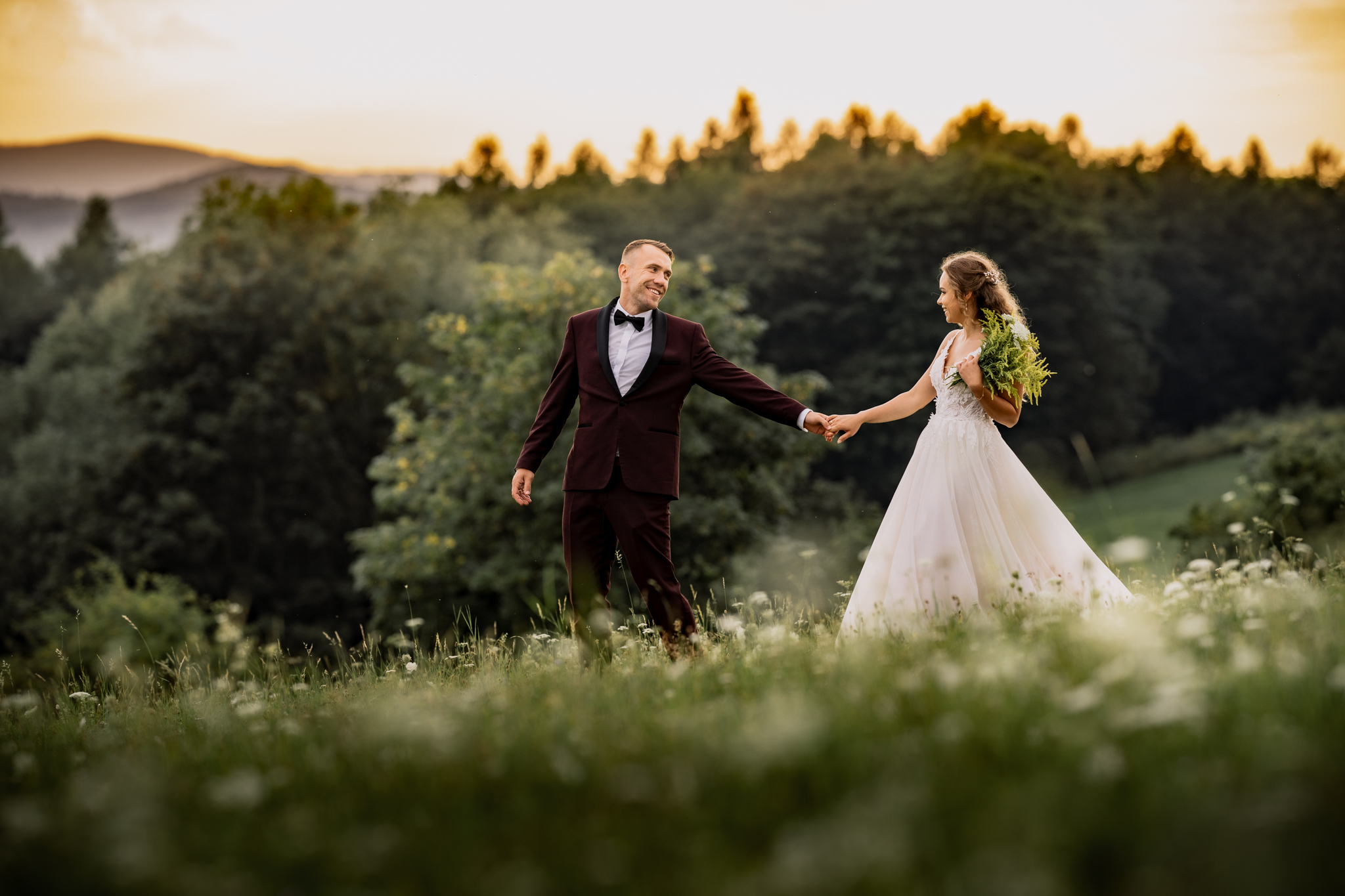 Kobieta i mężczyzna w ślubnych strojach idą łąką